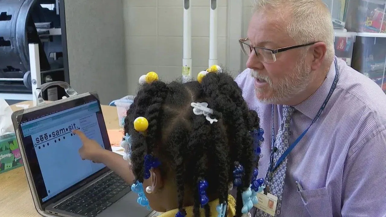A student pointing to a word on a laptop screen beside her instructor